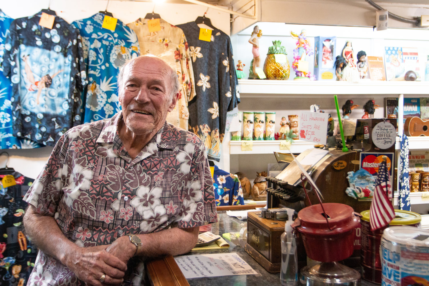 Pat Slusher, owner of Pat Slusher’s Coin Shop, poses with his antique register and wall full of Hawaiian items. At the age of 79, he plans to retire to his oceanside property and relax with his wife Phoebe.